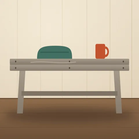 A low bench of weathered grey pallet boards with a green cushion and a red mug on it